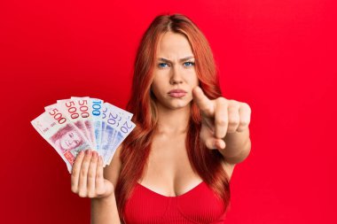 Elinde İsveç banknotları tutan güzel, kızıl saçlı bir kadın kamerayı işaret ediyor. Kendine güvenen bir jest, ciddi görünüyor. 
