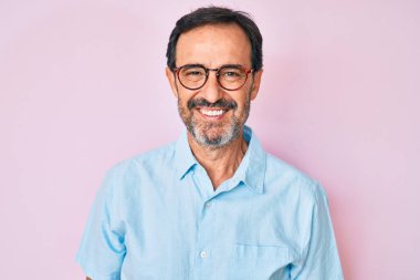 Orta yaşlı İspanyol bir adam günlük kıyafetler ve gözlük takıyor ve yüzünde mutlu ve havalı bir gülümseme var. şanslı kişi. 