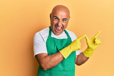 Olgun orta doğulu adam temiz önlük giyiyor ve eldivenler giyiyor gülümsüyor ve kameraya bakıyor iki eliyle ve parmaklarıyla kenarı işaret ediyor.. 