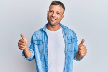 Sıradan kot ceket giyen yakışıklı kaslı adam elinde olumlu bir jest yapıyor, gülümsüyor ve mutlu. Neşeli ifade ve kazanan jest. 