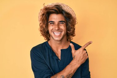 Yazlık şapkalı, neşeli, gülümseyen, elleri ve parmaklarıyla yüzünü gösteren, yüzünde mutlu ve doğal bir ifade olan İspanyol genç adam. 