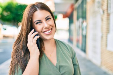 Genç İspanyol kadın gülümsüyor. Şehrin caddesinde yürüyen akıllı telefonla konuşuyor.