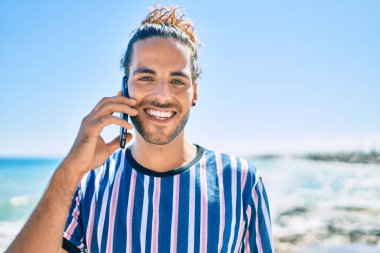 Genç İspanyol gülümseyen adam sahilde akıllı telefondan konuşarak mutlu oluyor..