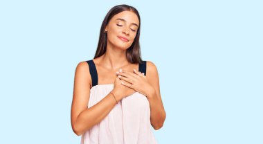 Gündelik kıyafetler giyen genç İspanyol kadın elleri göğsünde, gözleri kapalı ve yüzünde minnet dolu bir jest ile gülümsüyor. sağlık kavramı. 