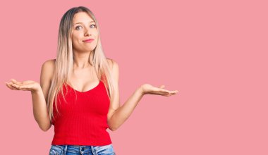 Genç, sarışın, sıradan kıyafetler giyen, kafası karışmış, kolları ve elleri havada genç bir kadın. şüphe kavramı. 