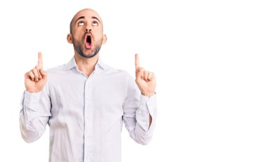 Zarif gömlek giyen genç yakışıklı adam şaşırmış ve şaşırmış bir şekilde yukarı bakıyor ve parmaklarıyla işaret ediyor ve kollarını kaldırıyor.. 