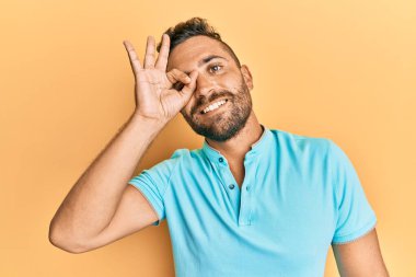 Sakallı, sıradan giyinen, gülümseyen, mutlu, el pençe divan duran yakışıklı bir adam. 