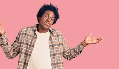 Afro saçlı, sıradan giyinmiş, gözlüksüz, kafası karışmış elleri ve kolları havada afro saçlı yakışıklı bir Amerikalı. şüphe kavramı. 