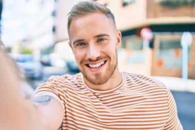 Genç İrlandalı gülümseyen adam şehrin caddesindeki kameranın önünde selfie çekerken mutlu oluyor..