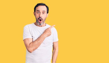 Gündelik tişört giyen orta yaşlı yakışıklı bir adam parmaklarını yana doğru göstererek şaşırdı, ağzı açık hayret içinde kaldı.. 