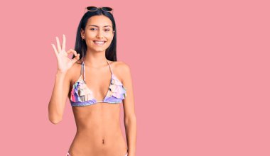 Bikini giyen, güneş gözlüklü, gülümseyen genç ve güzel Latin kız el ve parmaklarıyla 