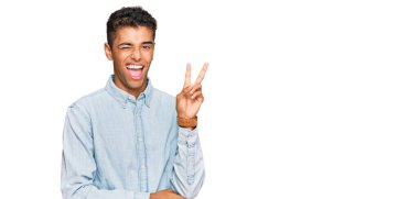 Genç, yakışıklı, Afro-Amerikalı sıradan kıyafetler giyen, gülümseyen, kameraya göz kırpan, zafer işareti yapan bir adam. İki numara.. 