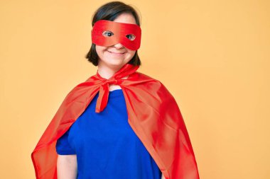 Down sendromlu esmer kadın süper kahraman kostümü giyiyor. Pozitif ve mutlu görünüyor. Kendine güvenen bir gülümsemeyle dişlerini gösteriyor. 