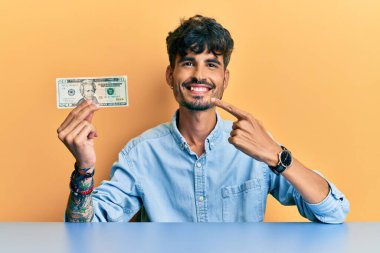 20 dolarlık banknot tutan genç İspanyol adam mutlu bir şekilde elini ve parmağını gösterdi. 