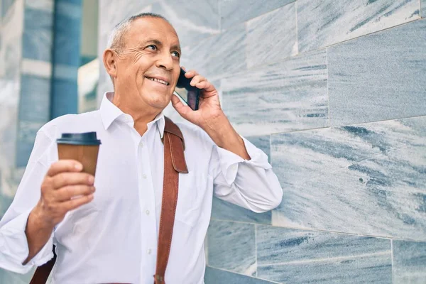 나이든 백발의 사업가가 스마트폰으로 커피를 마시며 도시에서 커피를 마시고 있습니다 — 스톡 사진