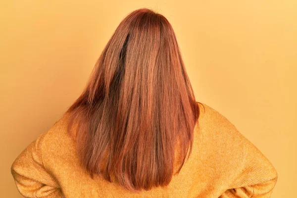 美丽的红头发女人 穿着宽松的冬季毛衣 背景是黄色的 背对着身体 向后看去 — 图库照片
