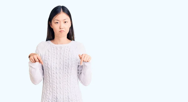 若い美しい中国の女性は 指で方向を示す 不幸なと落ち込んで 悲しいと動揺見て下を向いてカジュアルなセーターを着て — ストック写真