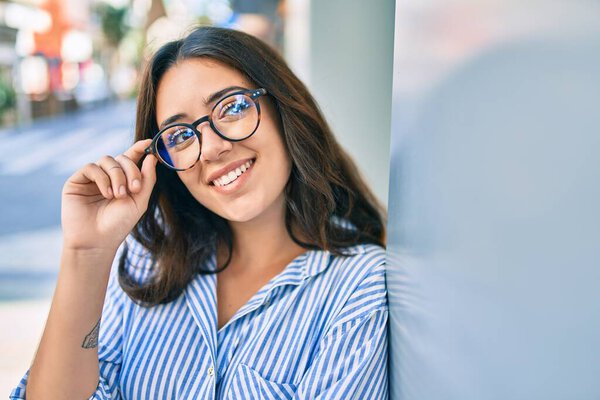 Young hispanic businesswoman smiling happy leaning on the wall at the city