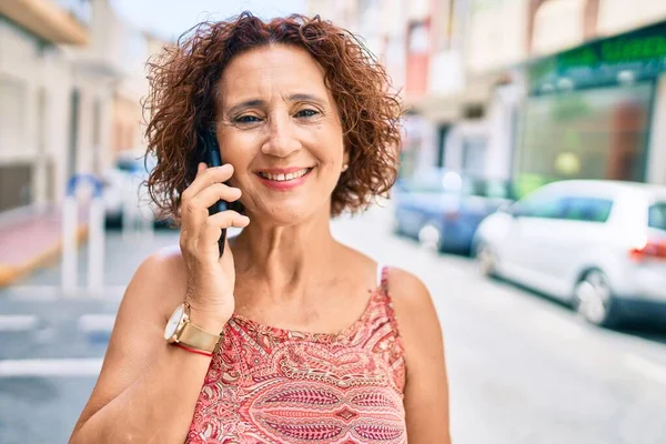 中年の女性が笑顔で幸せな話をスマートフォンで街の通りを歩く — ストック写真