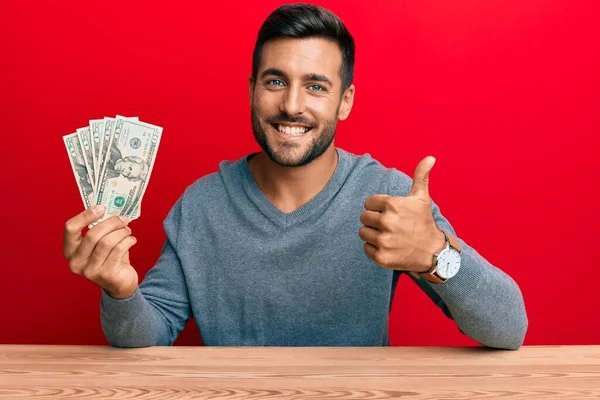 Hombre Hispano Guapo Sosteniendo Billetes Dólares Sonriendo Feliz Positivo Pulgar — Foto de Stock