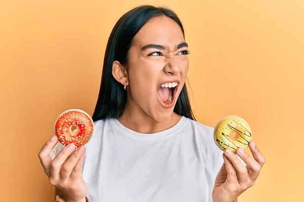 Mujer Asiática Joven Sosteniendo Sabrosas Rosquillas Coloridas Enojado Loco Gritando —  Fotos de Stock
