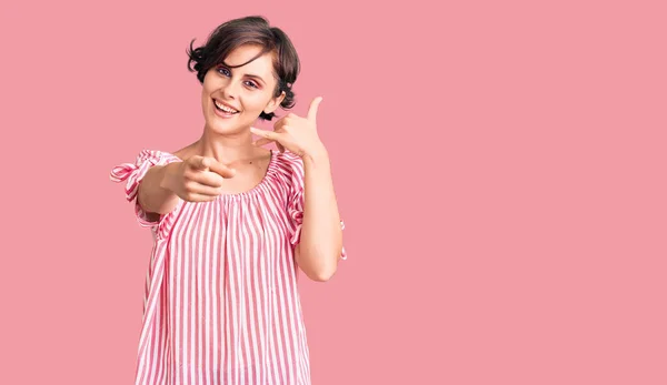 Beautiful young woman with short hair wearing casual summer clothes smiling doing talking on the telephone gesture and pointing to you. call me.