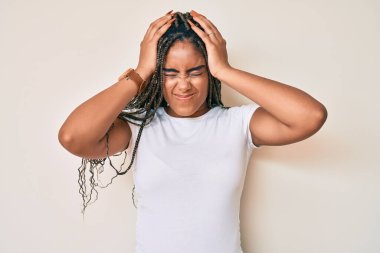 Saçları günlük beyaz tişörtler giyen, acı ve migren yüzünden çaresiz ve stresli genç Afro-Amerikalı bir kadın. Eller başının üstünde.. 