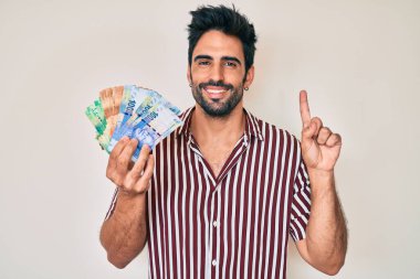 Sakallı yakışıklı İspanyol bir adam elinde Güney Afrika rand banknotları bir fikir veya soruyla gülümsüyor. 