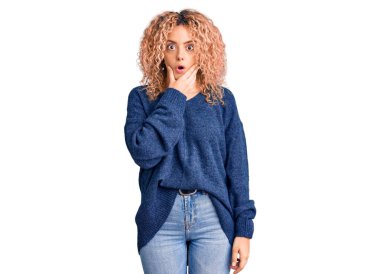 Kış süveteri giyen, kıvırcık saçlı genç sarışın kadın elleri çenesinde olan inançsızlıktan, şaşkınlıktan ve şaşkınlıktan büyülenmiş görünüyor. 