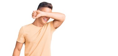 Genç ve yakışıklı bir adam günlük kıyafetler giyip gözleri kollarıyla kapatıp neşeli ve komik bir şekilde gülümsüyor. kör kavram. 