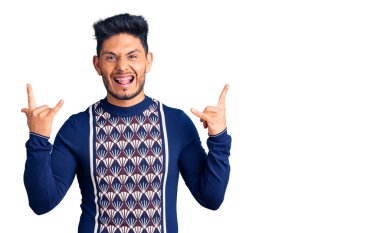 Yakışıklı Latin Amerikalı genç adam, günlük kışlık süveter giyip çılgın bir ifadeyle bağırıyor elleri havada rock sembolü yapıyor. Müzik yıldızı. ağır kavram. 