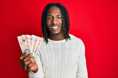 Saçları örgülü Afrika kökenli bir Amerikalı elinde 10 pound banknotla mutlu ve pozitif görünüyor ve gülümsüyor. 