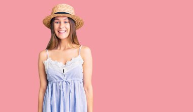 Güzel, esmer, yaz şapkası takan güzel bir kadın. Pozitif ve mutlu görünüyor. Duruyor ve gülümsüyor. 