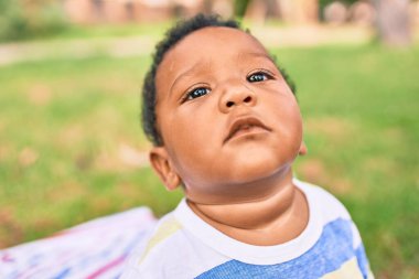 Sevimli Afro-Amerikan tombul çocuk parkta çimlerin üzerinde oturuyor..