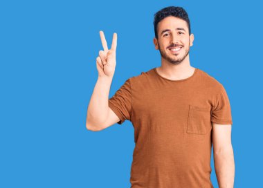 Gündelik kıyafetler giyen genç İspanyol adam iki numarayı gösterip işaret ederken kendinden emin ve mutlu bir şekilde gülümsüyor.. 