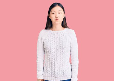 Gündelik süveter giyen genç, güzel Çinli bir kadın komik yüzlü yanakları şişiriyor. Havayla şişmiş ağız, çılgın bir ifade.. 