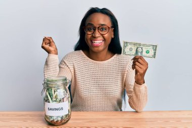 Genç Afrikalı bir kadın elinde dolar ve kavanozla gururla bağırıyor zaferi ve başarıyı kutluyor. 