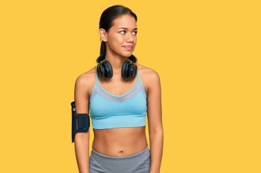 Güzel İspanyol kadın spor giyer ve kulaklık takar. Yüzünde gülümseme, doğal bir ifade ile yan yana bakar. Kendinden emin gülen. 