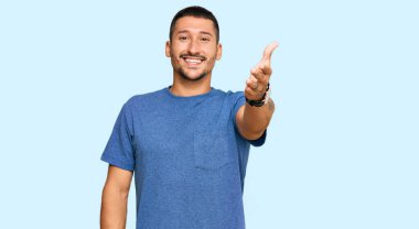 Sıradan kıyafetler giyen yakışıklı bir adam gülümseyerek selamlama ve hoş geldin demek için tokalaşıyor. başarılı iş. 