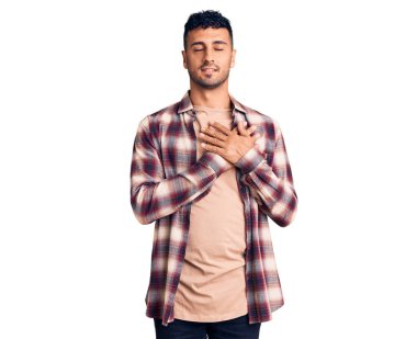 Gündelik kıyafetler giyen genç İspanyol adam elleri göğsünde, gözleri kapalı ve yüzünde minnet dolu bir jest ile gülümsüyor. sağlık kavramı. 
