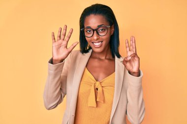 Genç afro-amerikan kadın iş kıyafetleri giyer ve 8 numaralı parmaklarıyla işaret ederken kendinden emin ve mutlu gülümser.. 
