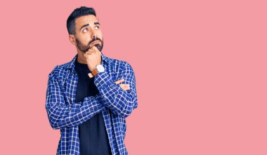 Elleri çenesinde gündelik giysiler içinde soru soran genç İspanyol bir adam, düşünceli bir ifade. Düşünceli bir yüzle gülümsüyor. şüphe kavramı. 