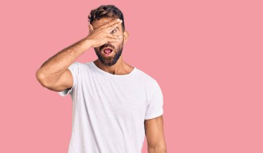 Gündelik beyaz tişört giyen genç İspanyol adam şok içinde yüzünü ve gözlerini kapayarak utangaç ifadesiyle parmaklarının arasından bakıyor.. 