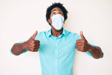 Yakışıklı Afro saçlı, tıbbi maske takan, sinirli ve öfkeli sinirli sinirli sinirli, öfkeyle bağıran, öfkeyle bakan afro-amerikalı bir adam.. 