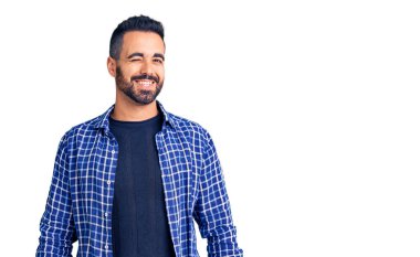 Gündelik kıyafetler giyen genç İspanyol adam kameraya seksi bir ifadeyle bakıyor, neşeli ve mutlu bir yüzle.. 