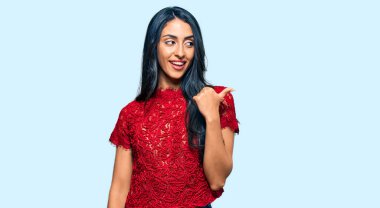 Zarif bir tişört giyen güzel İspanyol kadın mutlu yüzle gülümsüyor ve başparmağıyla yan tarafı işaret ediyor.. 