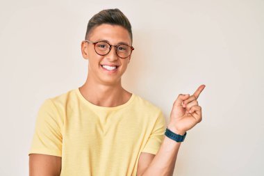 Gündelik kıyafetler ve gözlük takan genç İspanyol çocuk gülümsüyor mutlu bir şekilde elini ve parmağını yana uzatıyordu. 