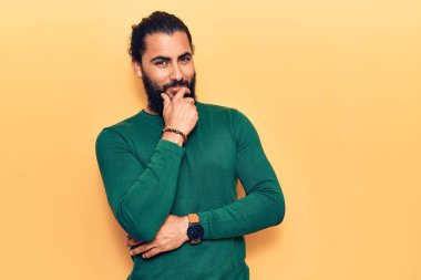 Gündelik giysiler giyen genç Arap adam kameraya kollarını kavuşturup çenesine dokunarak gülümsüyor. Olumlu düşünmek. 