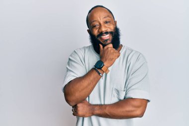 Sıradan kıyafetler giyen genç Afro-Amerikan bir adam kameraya kollarını kavuşturup, çenesini kapatarak gülümsüyor. Olumlu düşünmek. 