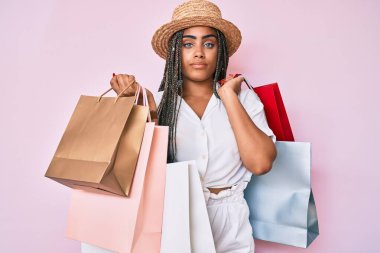 Saçları örülü, alışveriş torbaları tutan genç Afro-Amerikalı kadın yüzünde ciddi bir ifadeyle rahatlamış. Basit ve doğal bir şekilde kameraya bakıyorsun.. 